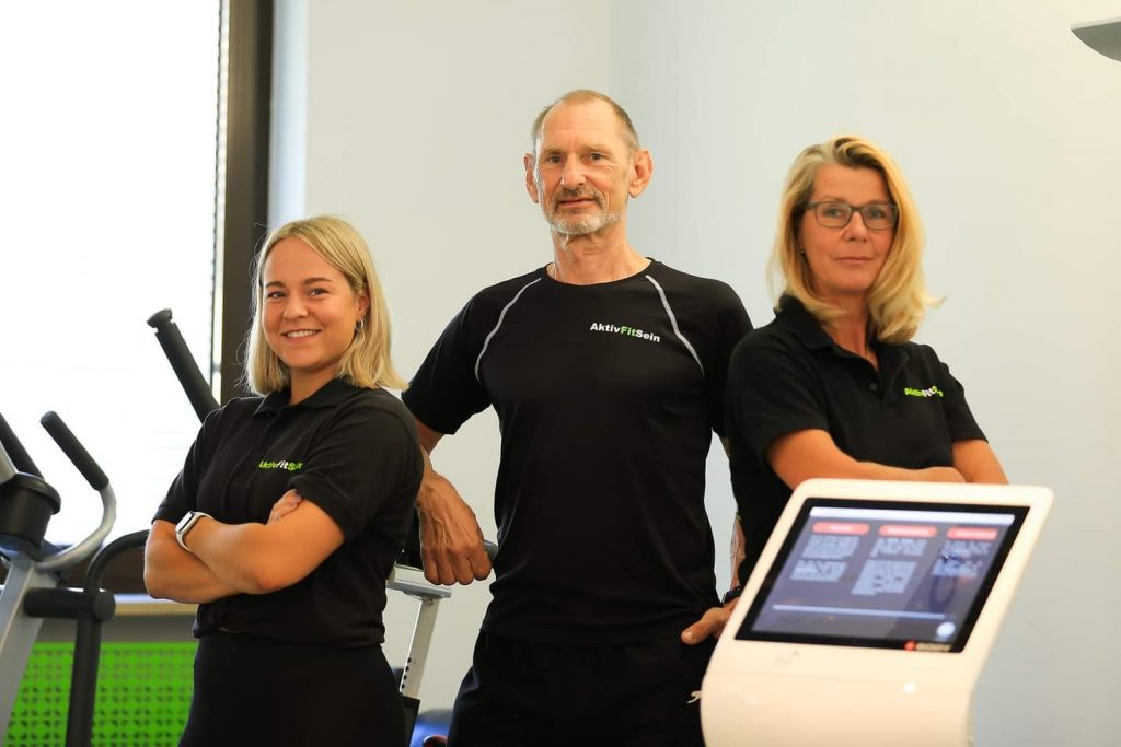 Das Team von Aktiv-Fit-Sein in Zirndorf steht zusammen vor dem EMS X-body gerät und verkörpert Firmenfitness.