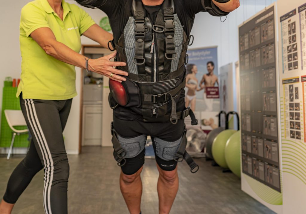 Ein Mann führt bei Aktiv Fit Sein in Zirndorf eine Übung mit einem Suspension-Trainer während eines EMS-Trainings durch. Eine Trainerin unterstützt ihn dabei.